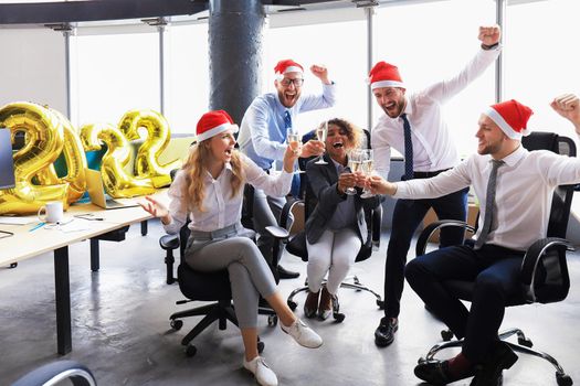 Business people are celebrating holiday in modern office drinking champagne and having fun in coworking. Merry Christmas and Happy New Year 2022