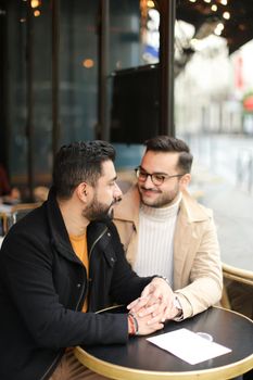 Two european handsome gays talking at street cafe and holding hands. Concept of same sex couple and lgbt.