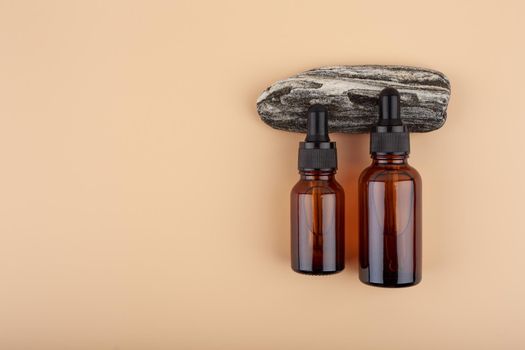 Two dark transparent glass bottles with skin serum or oil for manicure on black natural stone against bright beige background with copy space. Concept of luxury skin care products