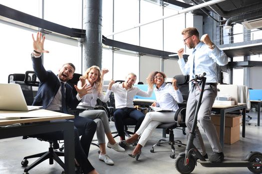 Five happy modern business people are keeping arms raised and expressing joyful while sitting in large office