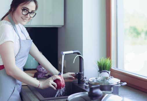 Woman washing vegetables. Beautiful young woman washing vegetables for salad and smiling while standing in the kitchen.