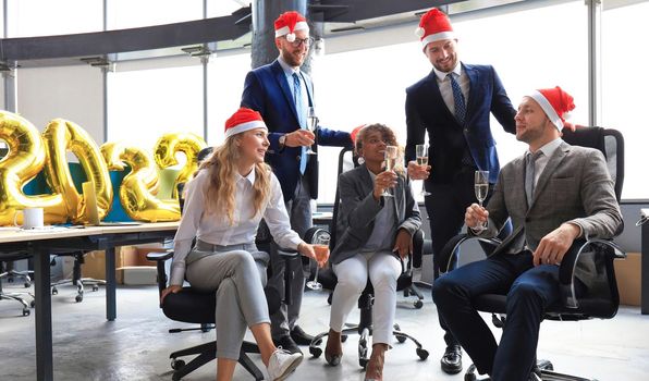 Business people are celebrating holiday in modern office drinking champagne and having fun in coworking. Merry Christmas and Happy New Year 2022