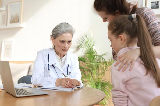 Mother and child in the doctor office meeting the pediatrician, they are sitting at desk in hospital