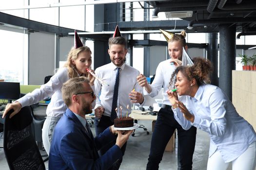 Happy business team with birthday cake are greeting colleague at office party.