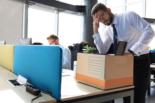 Sad dismissed worker are taking his office supplies with him from office.