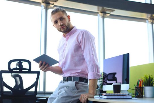 Young modern business man working using digital tablet while sitting in the office