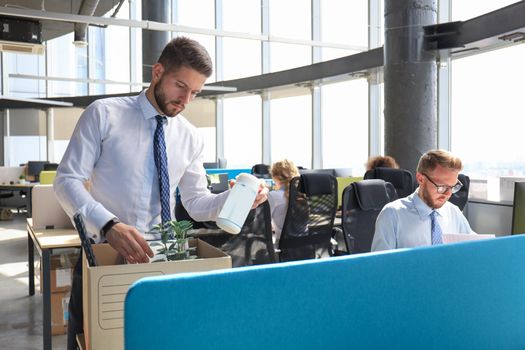 Sad dismissed worker are taking his office supplies with him from office.