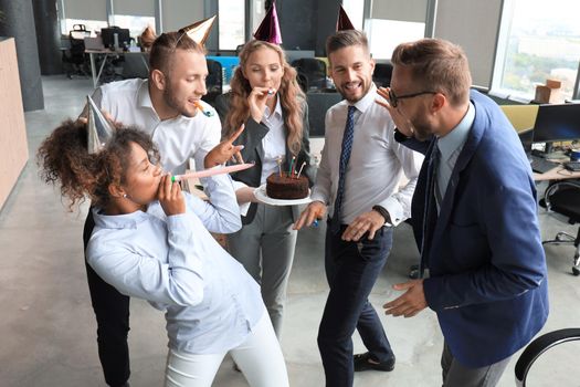 Happy business team with birthday cake are greeting colleague at office party.