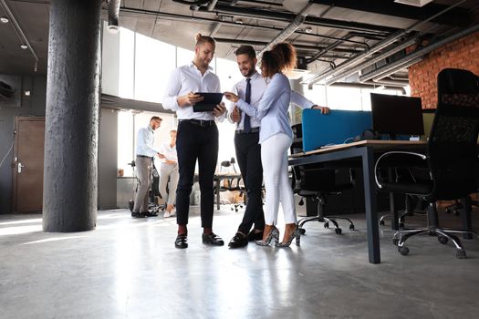 Group of modern business people are talking and smiling while standing in the office hallway.