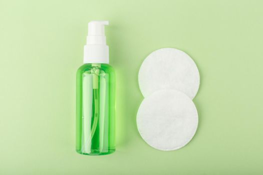 Top view of green organic cleansing foam or gel for make up removing in transparent tube and cotton pads on bright green background. Concept of daily skin care or anti acne treatment