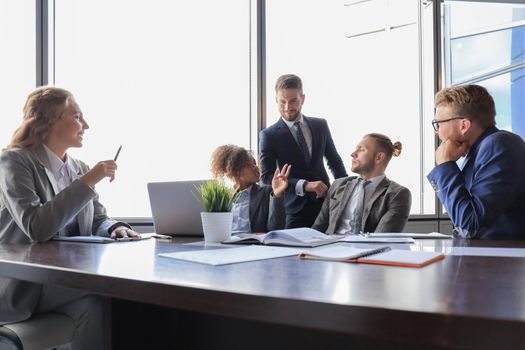 Group of young modern people in formalwear smiling and discussing something while working in the modern office.