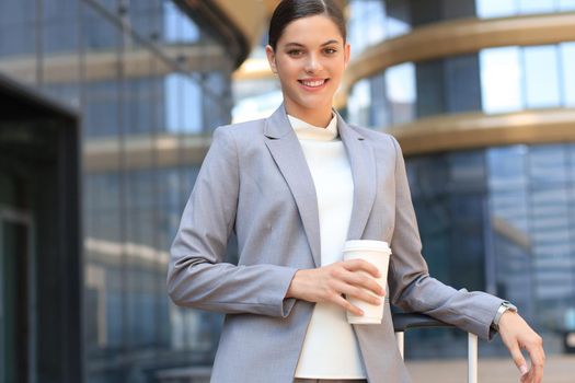 Portrait of successful business woman going to work with coffee walking near office building on city street