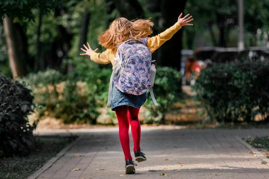 Preteen school girl with backpack running after class, back view. Pretty pupil female kid in autumn park