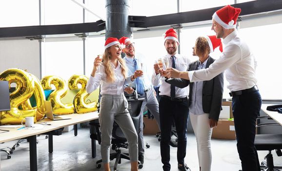 Business people are celebrating holiday in modern office drinking champagne and having fun in coworking. Merry Christmas and Happy New Year 2022