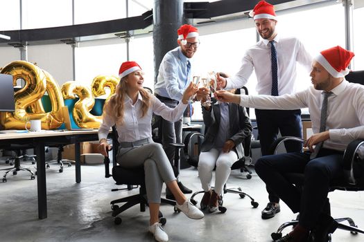 Business people are celebrating holiday in modern office drinking champagne and having fun in coworking. Merry Christmas and Happy New Year 2022