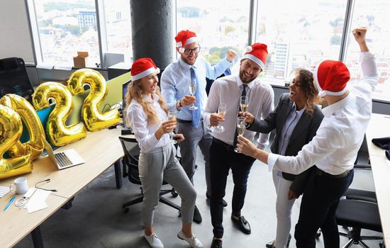 Business people are celebrating holiday in modern office drinking champagne and having fun in coworking. Merry Christmas and Happy New Year 2022