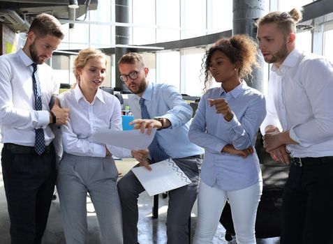 Group of modern business people are talking and smiling while standing in the office.