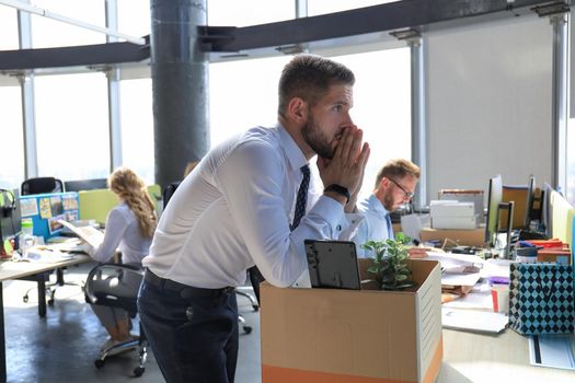 Sad dismissed worker are taking his office supplies with him from office.