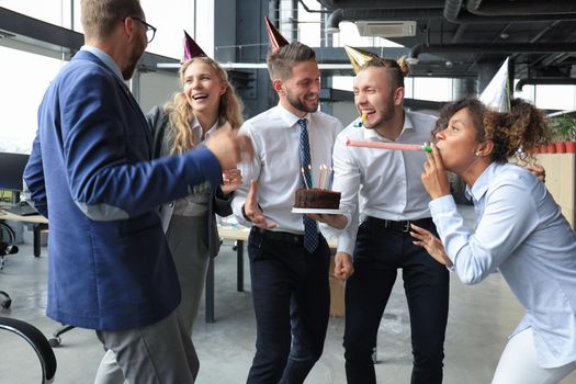 Happy business team with birthday cake are greeting colleague at office party.
