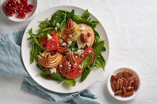 Fruits citrus salad with nuts, green lettuce leaves. Balanced food. Spinach with orange, grapefruit, apples, pecans and gorgonzola, garnished with pomegranate seeds on table with white tablecloth.