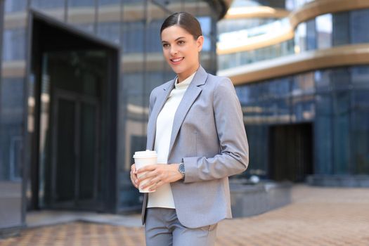 Portrait of successful business woman going to work with coffee walking near office building on city street