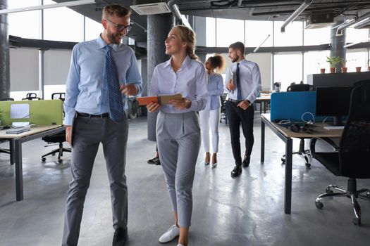 Group of modern business people are talking and smiling while standing in the office hallway.