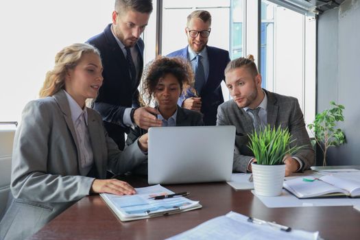 Group of young modern people in formalwear smiling and discussing something while working in the modern office.
