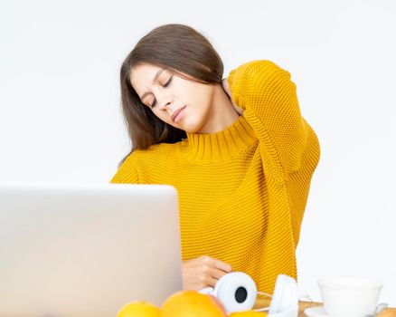 Woman massaging neck pain from working at computer for long time. Beautiful young lady in bright yellow jumper sitting at Desk