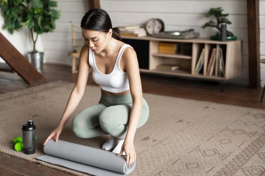 Asian fitness girl finish training,workout at home, rolling floor mat after exercising in living room, cleaning.