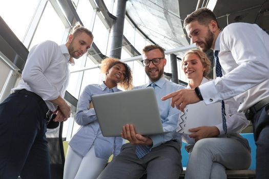 Group of modern business people are working using laptop and smiling while standing in the office hallway.