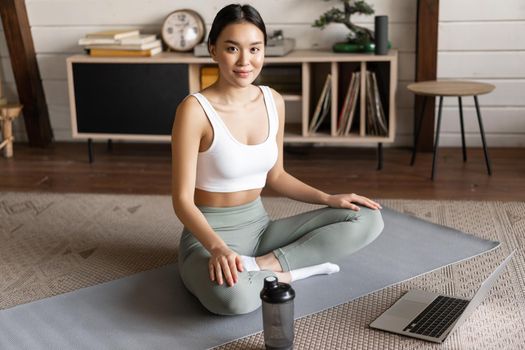 Young asian woman doing yoga with laptop, listening to meditation instructor on application or website, doing meditating course at home.