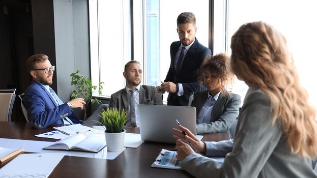 Group of modern business people in formalwear discussing business and smiling while sitting in the office.
