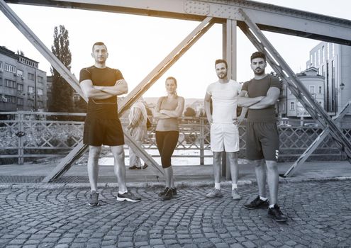 group of young sporty people jogging across the bridge at sunny morning in the city