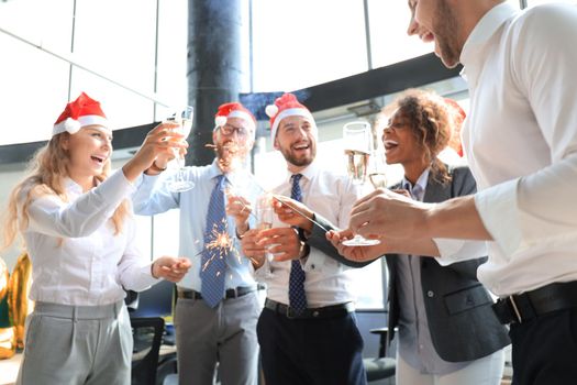 Young business partners are lighting bengal lights and drinking champagne in a modern office. Merry Christmas and Happy New Year
