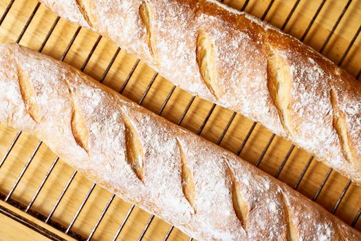 Fresh baked homemade crusty bread baguette. Two loaves cool on metal grate on wooden table. Delicious and healthy homemade loaf. Close up