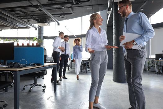 Group of modern business people are talking and smiling while standing in the office hallway.