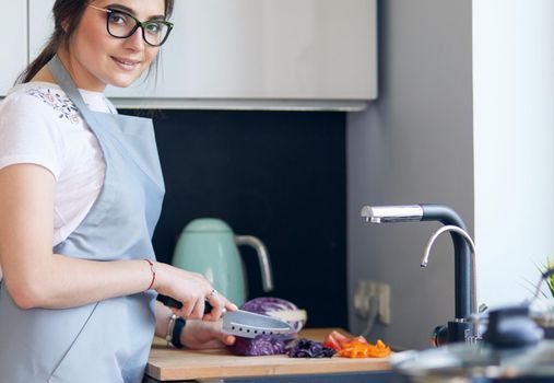 Young woman cutting vegetables in kitchen standing near desk.