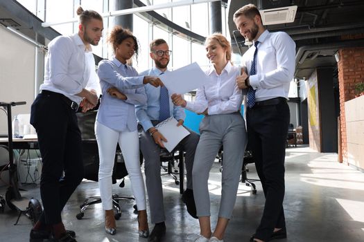 Group of modern business people are talking and smiling while standing in the office.