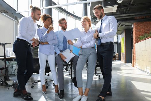Group of modern business people are talking and smiling while standing in the office hallway.