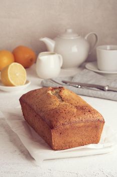 Lemon bread. Cake with citrus and poppy on cutting board, traditional american cuisine. Whole loaf. White background, gray table. Vertical, side view, copy space