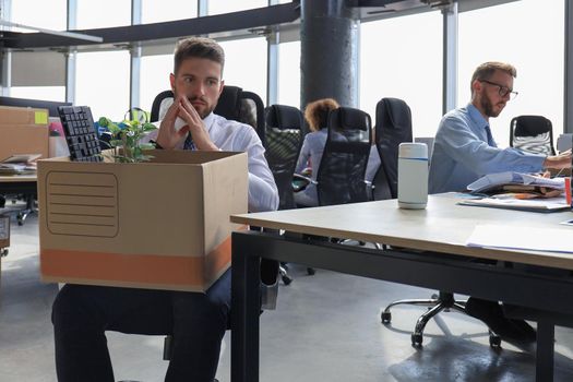 Sad dismissed worker are taking his office supplies with him from office.