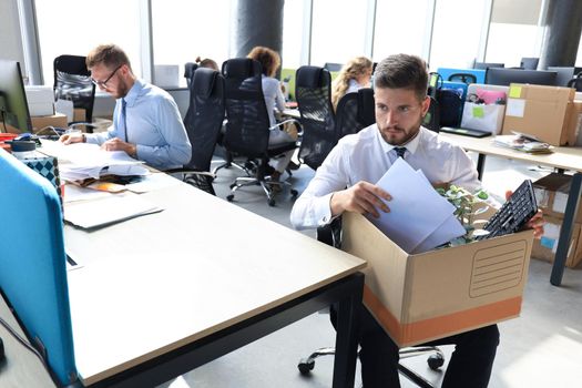 Sad dismissed worker are taking his office supplies with him from office.