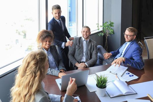 Group of young modern people in formalwear smiling and discussing something while working in the modern office.