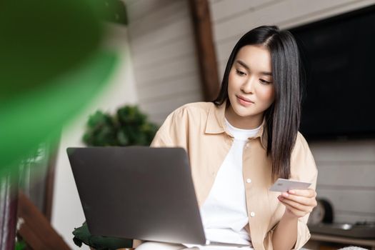 Portrait of asian girl buying on website with laptop and credit card. Young woman purchase online, sitting at home and shopping in internet.