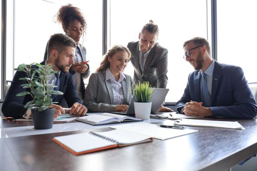 Group of young modern people in formalwear smiling and discussing something while working in the modern office.