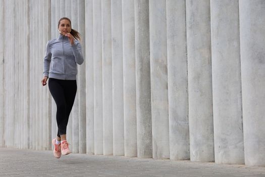 Full length of young sporty woman jogging while exercising outdoor.
