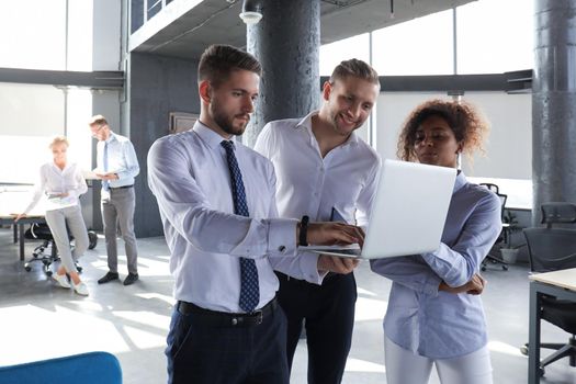 Group of modern business people are working using laptop and smiling while standing in the office hallway.