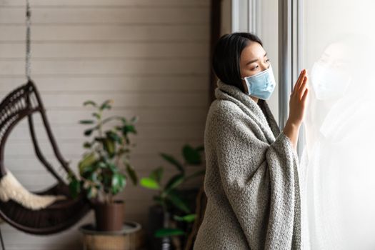 Sick asian woman staying at home on quarantine from covid-19, wearing face mask, looking out of window, yearning go outside.