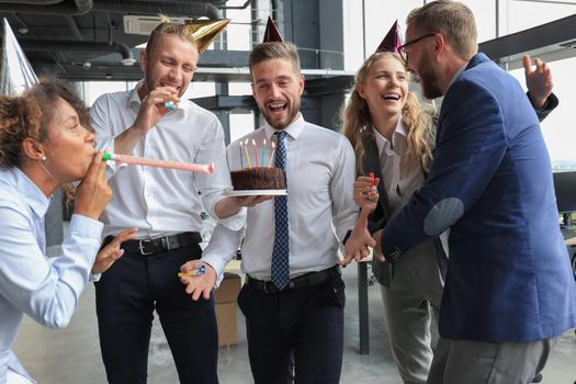 Happy business team with birthday cake are greeting colleague at office party.