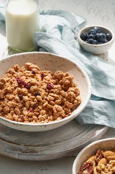 Dry granola in bowl. Breakfast, sunny morning, hard light, white table. Side view, vertical